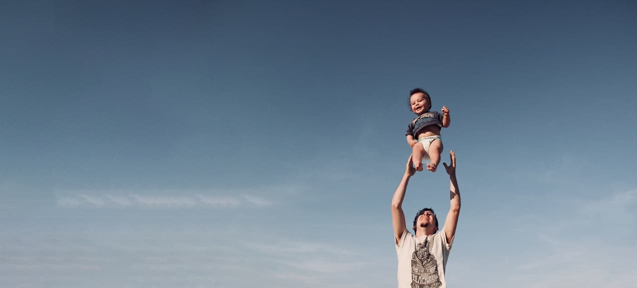 A father joyfully lifting his child into the air against a clear sky, representing Shop On Fire’s Co-Parenting Coaching program that strengthens family dynamics for healthier parenting.