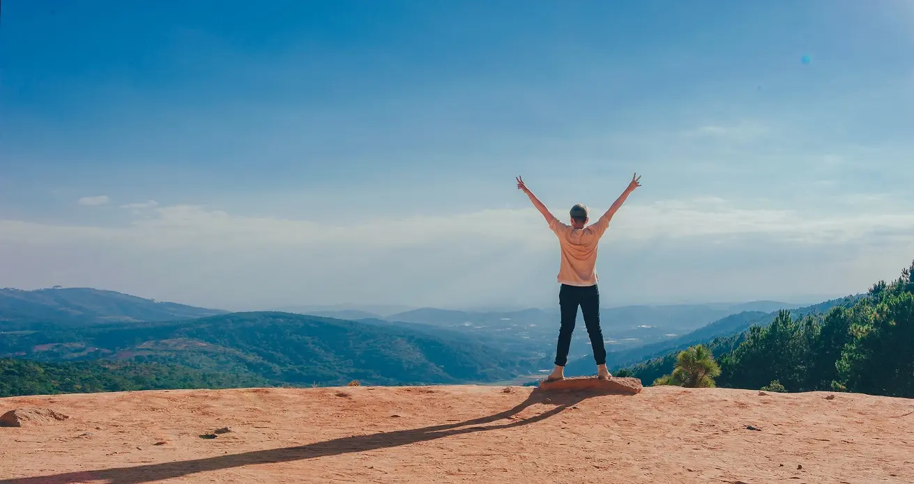 Person standing on a mountaintop with arms raised in victory, symbolizing the empowerment and renewal gained through Shop On Fire’s Divorce Coaching program.