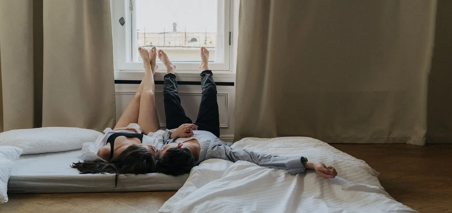 A couple lying on a bed, facing a window, symbolizing intimacy and connection, representing Shop On Fire’s Find a Better Mate Coaching program for healthier, stronger relationships.