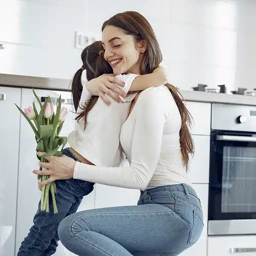 A joyful single mother embraces her child, holding a bouquet of tulips, symbolizing love, appreciation, and the spirit of Mother's Day. Highlighting Jeremiah Webb's campaign to deliver gift baskets to single moms.
