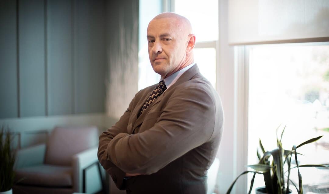 Jeremiah Webb, founder of Shop On Fire, standing confidently with arms crossed in a modern office, symbolizing his leadership and expertise in business growth and personal development coaching.