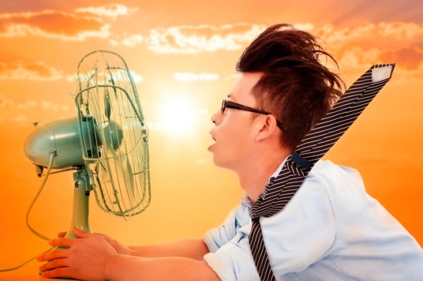 Man with his face close to an electric fan on a hot summer day, trying to stay cool while waiting for HVAC service, representing the importance of technician sales training during busy seasons.